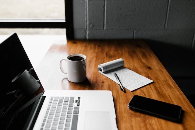 Desk with an open laptop, phone, coffee cup, and notpad